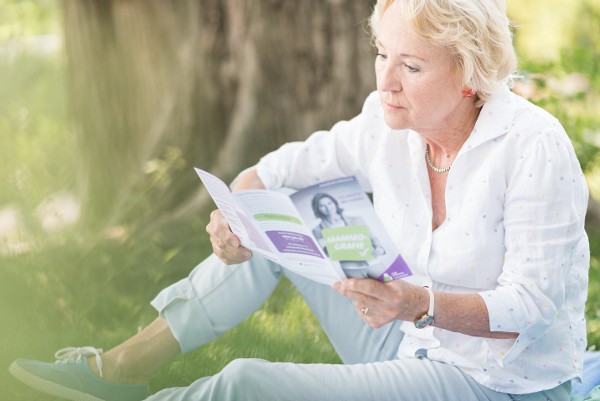 Frau sitzt am Rasen und liest Folder der Brustkrebsfrüherkennungsprogramms / Credit: asoluto/Angelika Schiemer