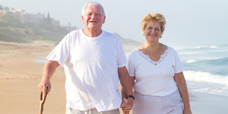 Alter Mann mit Holzgehstock und Frau beim Händchen halten am Strand. © shutterstock Inc.