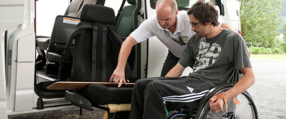 Ein Therapeut übt mit dem Patienten im Rollstuhl den Transfer auf einen Autositz mit Hilfe eines langen Rutschbrettes  