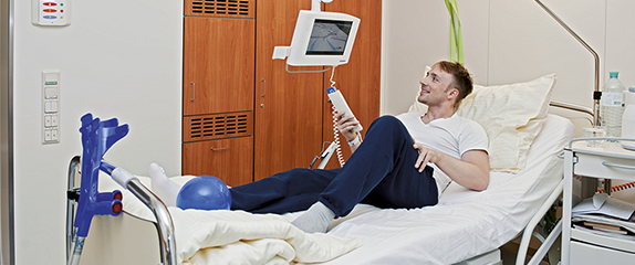 Liegender Patient bedient den am Bett montierten Monitor.