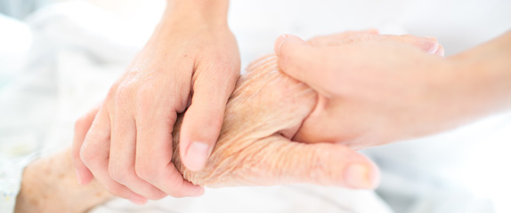 Eine ältere Hand wird gehalten von zwei Händen.