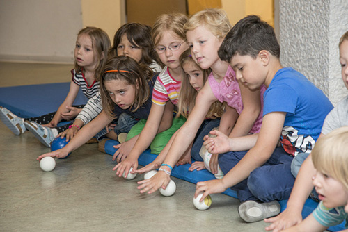 Kindergartenkinder rollen mit der Handfläche Bälle am Boden