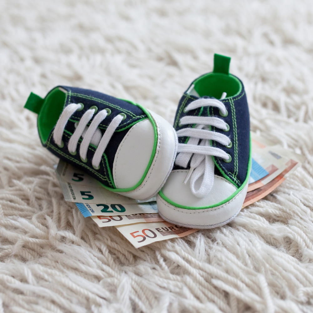 Babyschuhe und Geldscheine auf Teppich / Credit: bp-photographie.de/shutterstock.com
