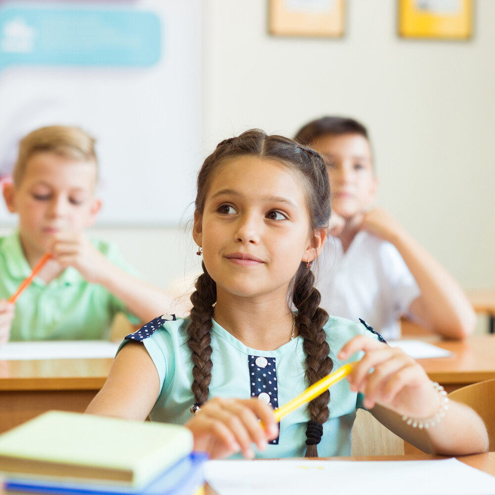 Kind sitzt in der Schule mit Stift in der Hand